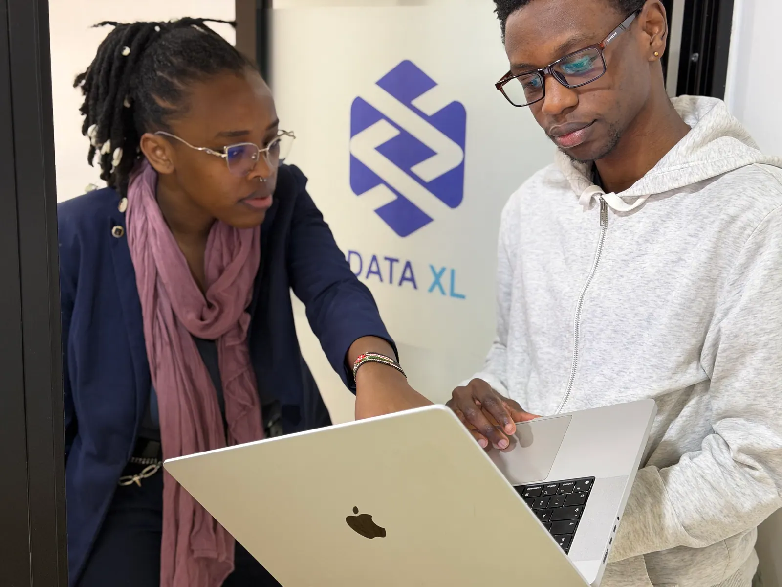Two Data XL colleagues reviewing work on a laptop, the Data XL mark on the wall behind them