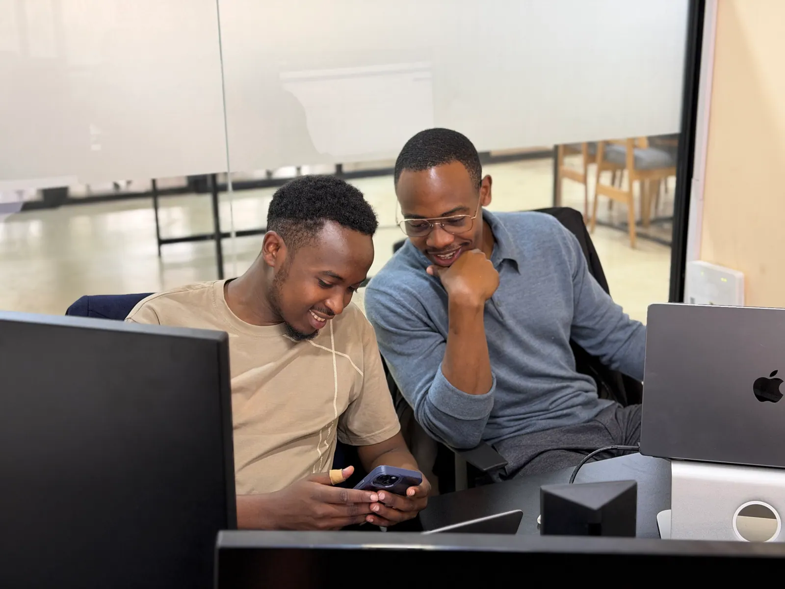 Two Data XL colleagues at their desks, laughing over something on a phone between them